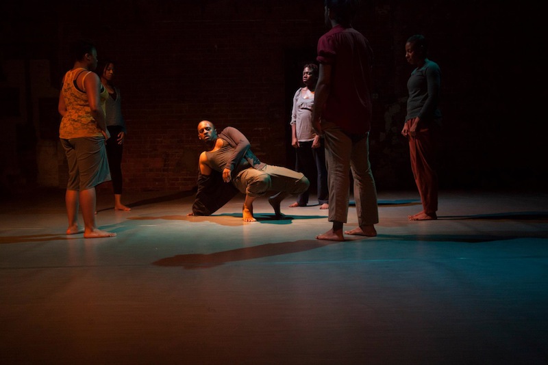 Members of Harge Dance Stories perform in dim lighting. The central male figure is on the floor 